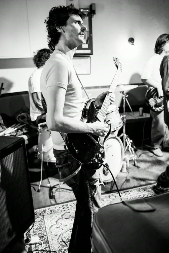 Cutthroat Kelly live: a guitarist in profile with a black guitar, the band setting up behind