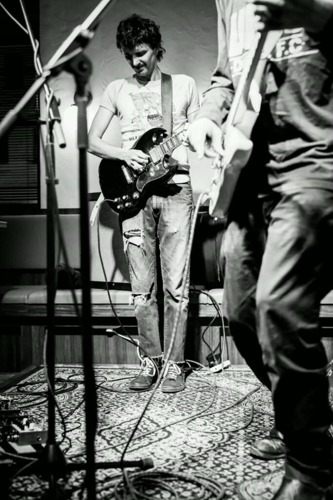 Cutthroat Kelly live: a guitarist with a black SG on a rug-covered stage